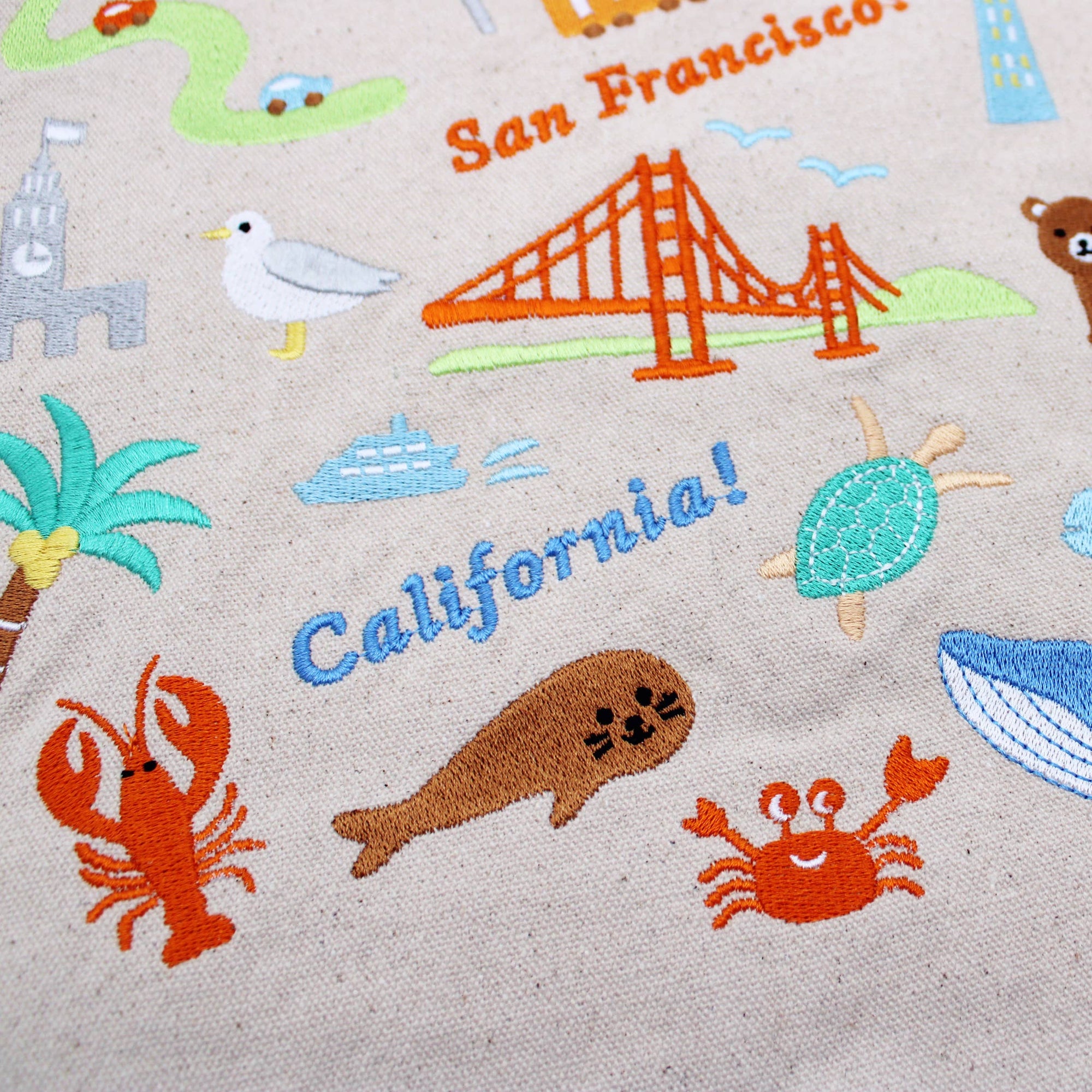 Fabric with embroidered elements of San Francisco, California, including the Golden Gate Bridge, seagull, palm tree, and sea creatures.