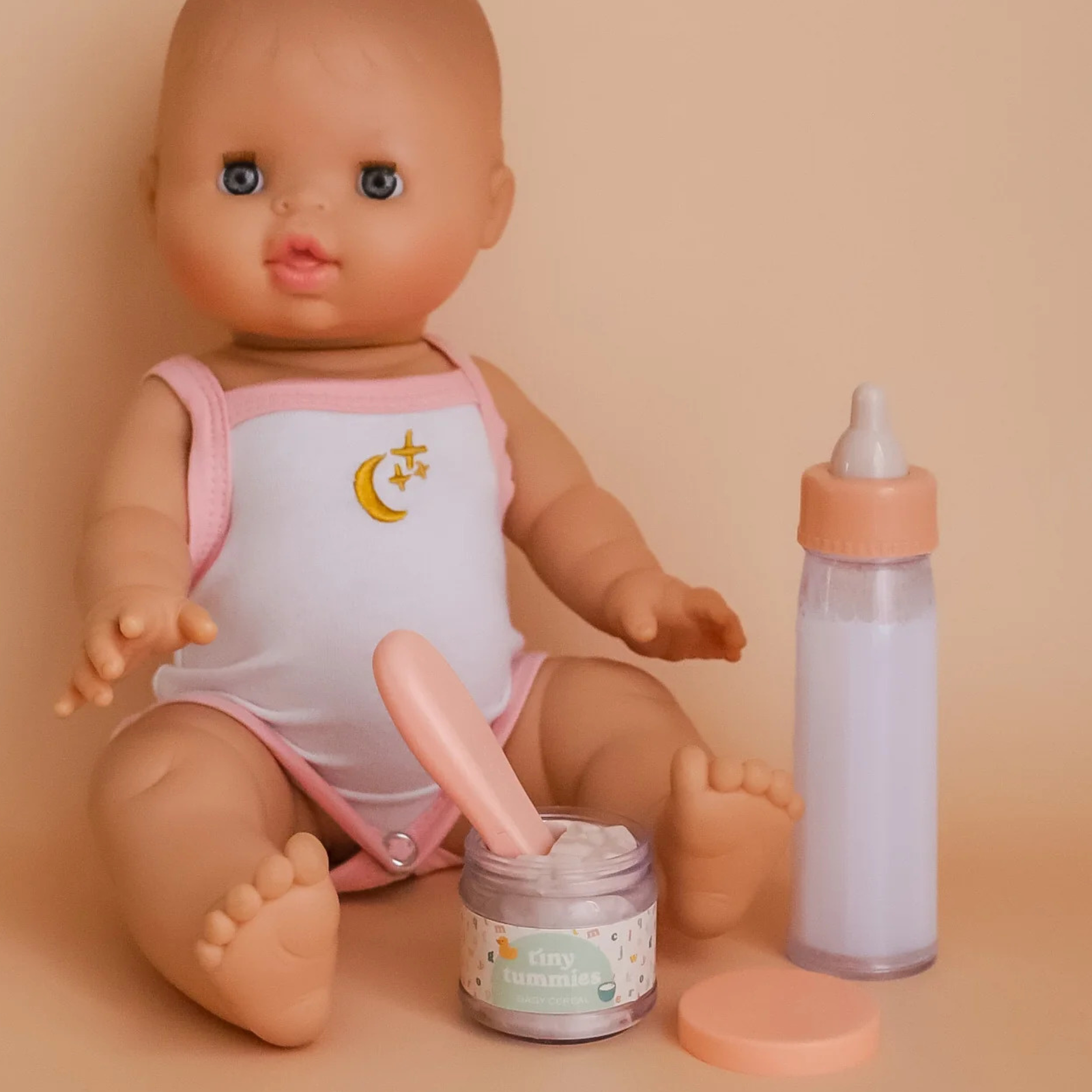 Baby doll with a bottle, jar, and pink outfit on a beige background