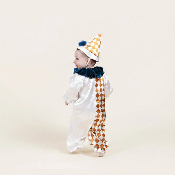 A baby wearing a white clown costume with a gold and white checkered hat, blue velvet collar, and matching checkered back panel, photographed against a plain cream background.