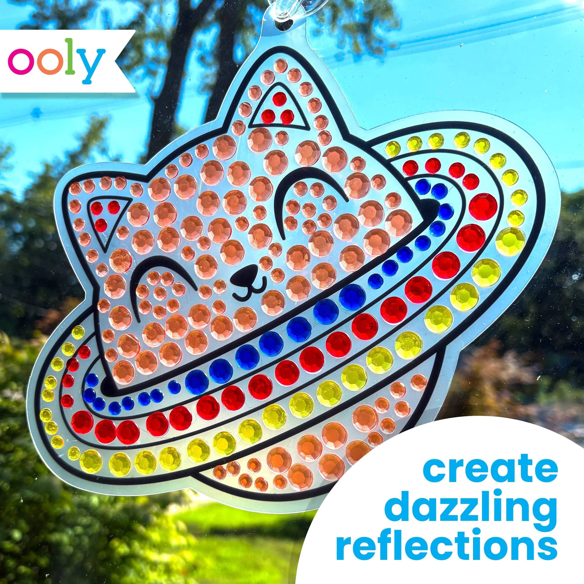 Decorative cat-shaped suncatcher with colorful dots on a window, featuring the brand 'ooly'.