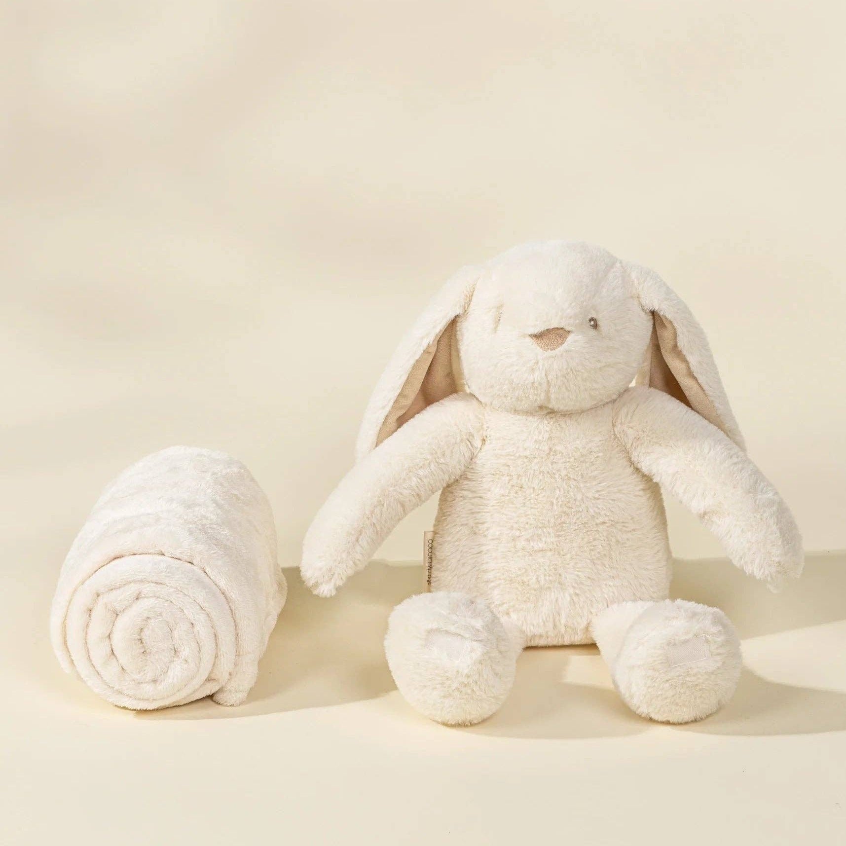 White plush bunny toy next to a rolled-up white blanket on a beige background