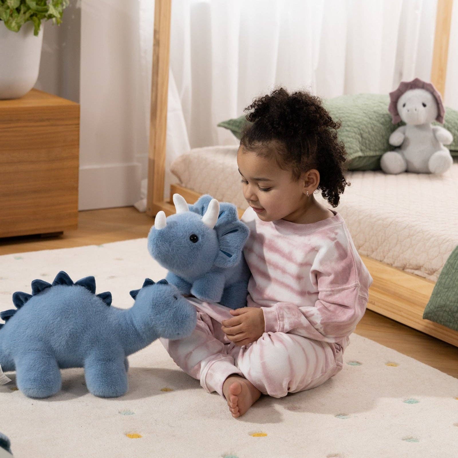 Child playing with blue dinosaur toys on a rug in a room with curtains and a plant.