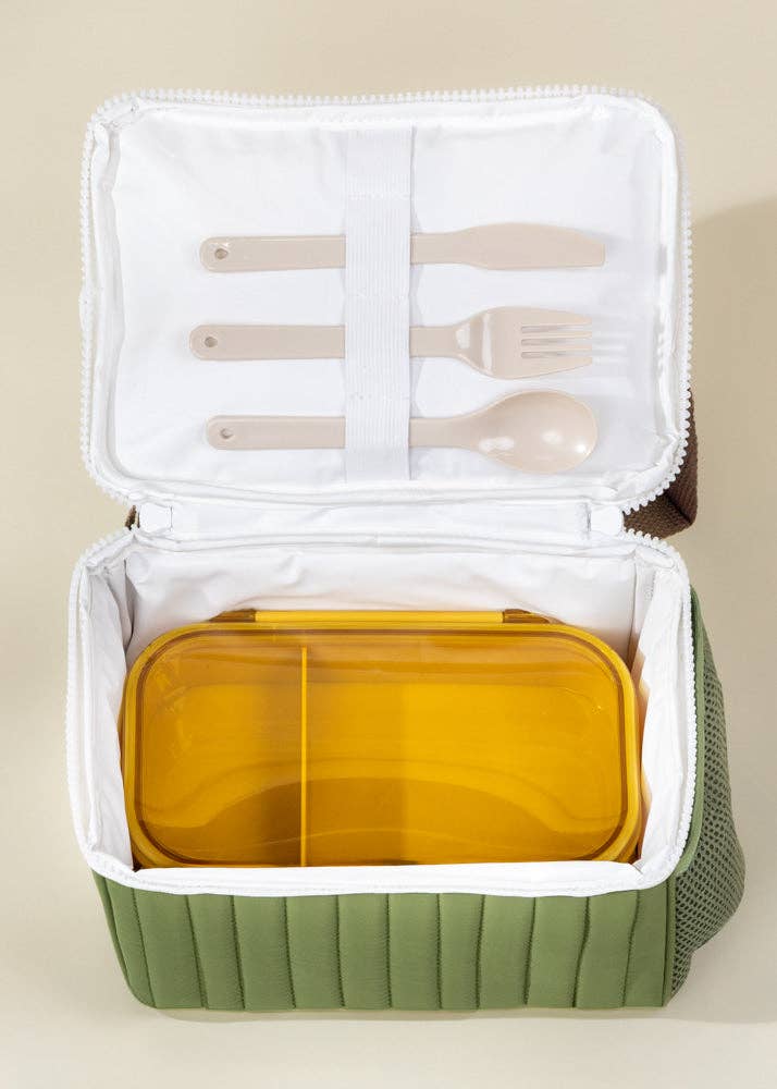 Green lunch box with compartments and utensils on a beige background