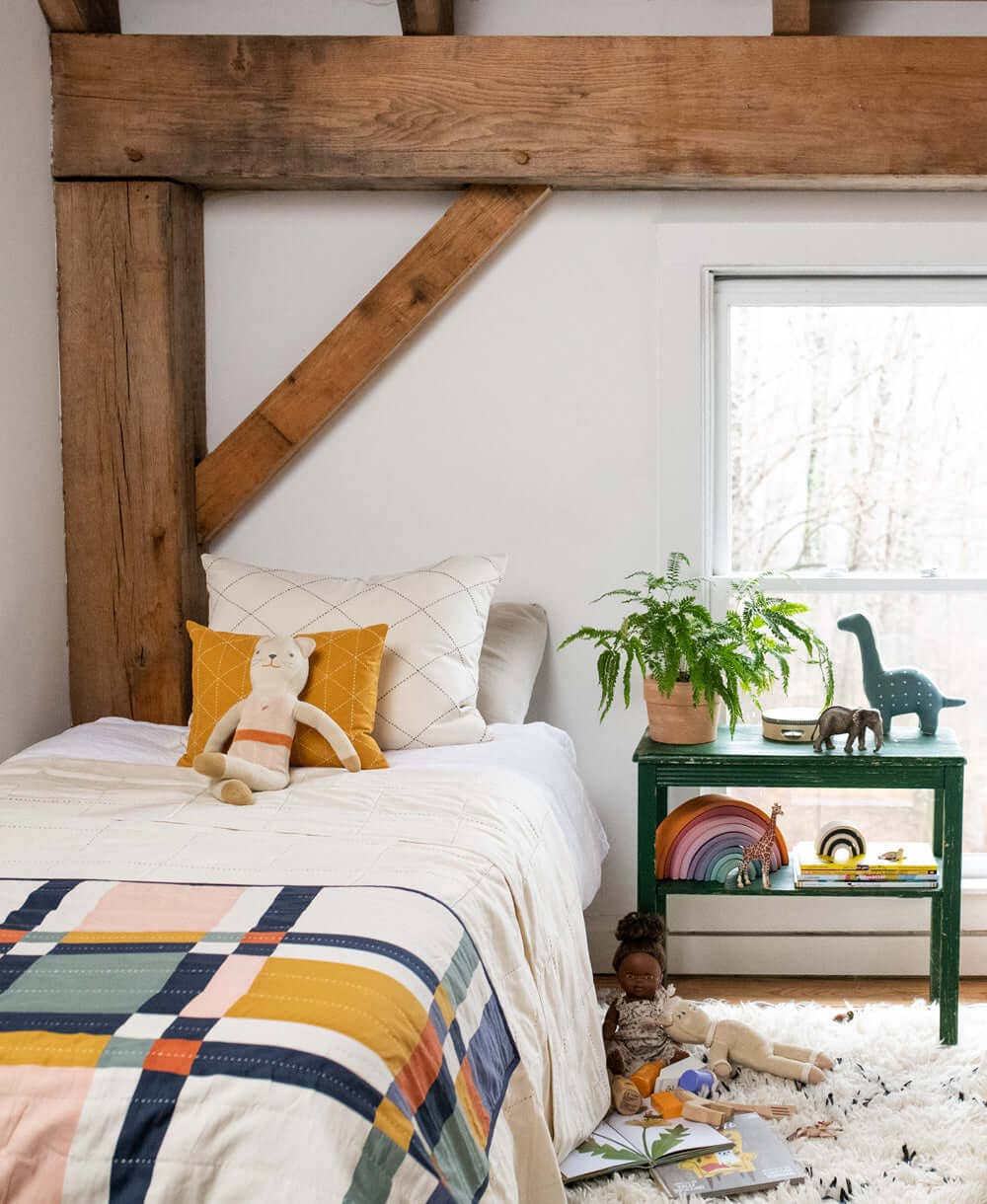 Children's bedroom with wooden beams, colorful bedding, and a nightstand with toys.
