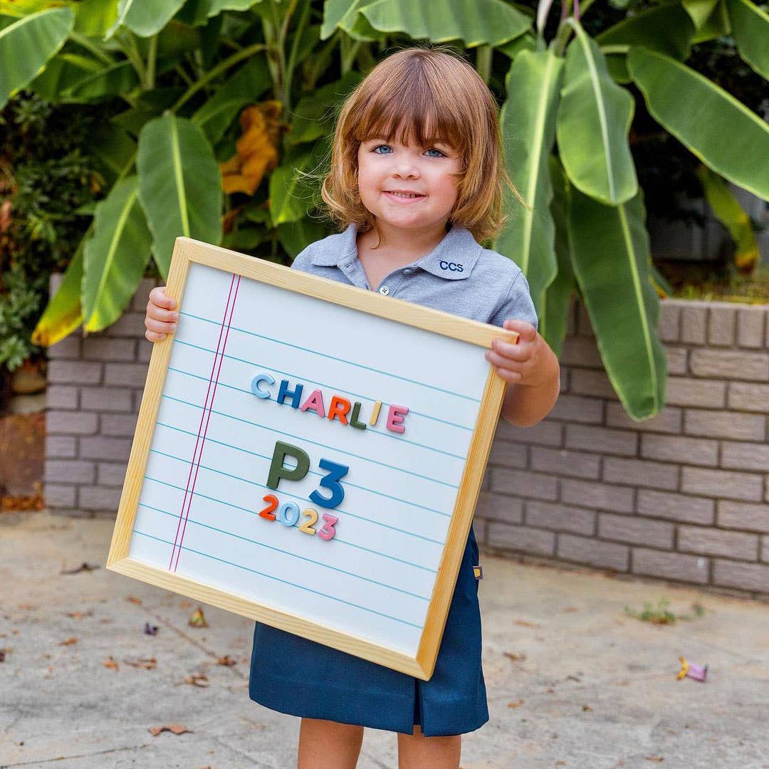 Child holding a letter board with 'CHARLIE P3 2023' outdoors