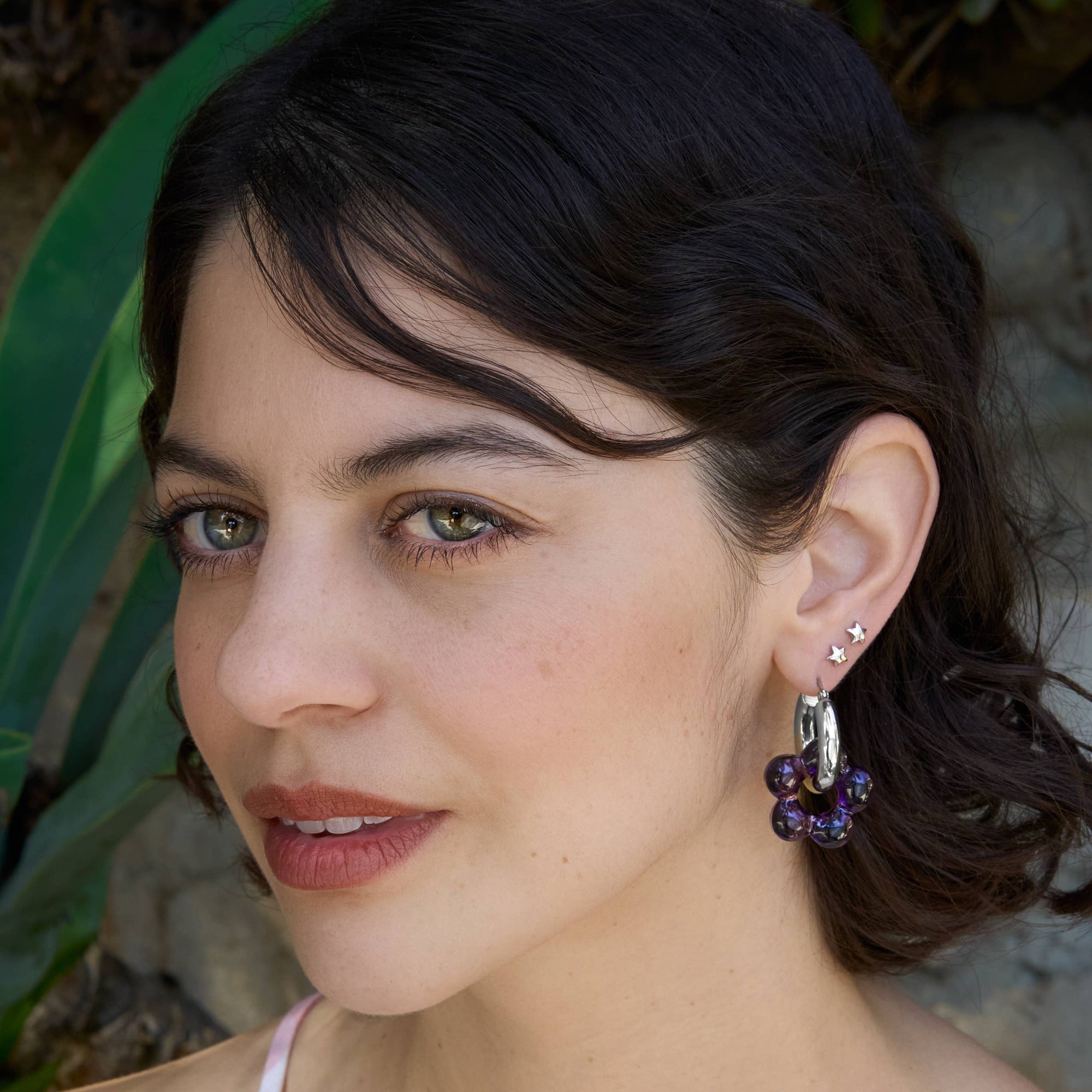 Woman wearing a pink checkered top with earrings outdoors