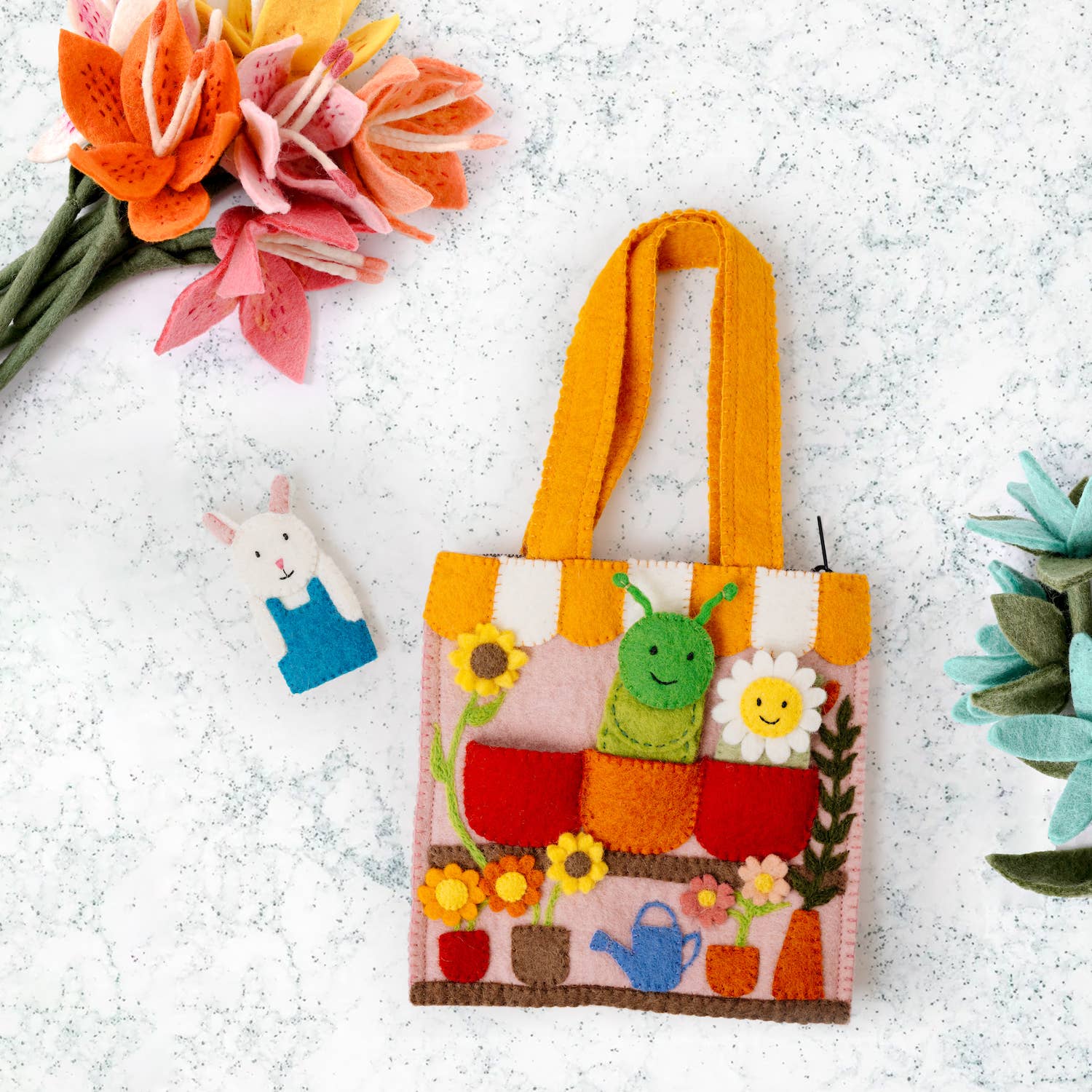 Colorful children's tote bag with garden design on a textured surface with flowers and a rabbit figurine.