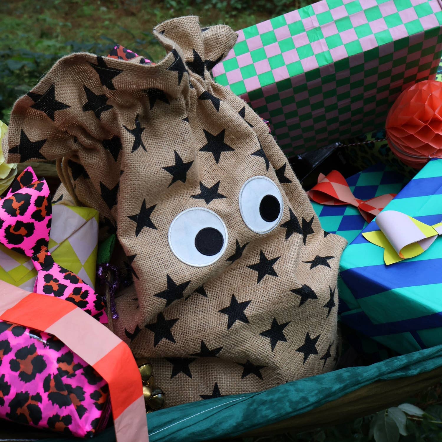 Star-patterned drawstring bag with googly eyes among colorful gift boxes and ribbons.