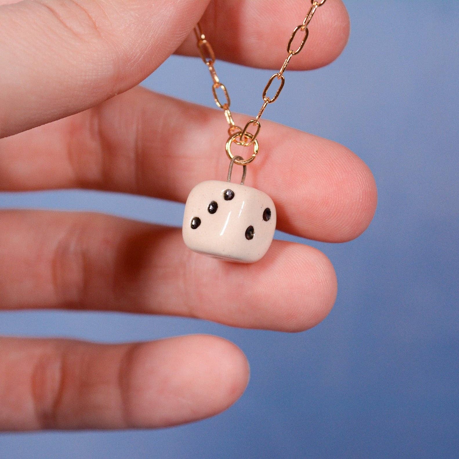 Hand holding a necklace with a dice-shaped pendant against a blue background
