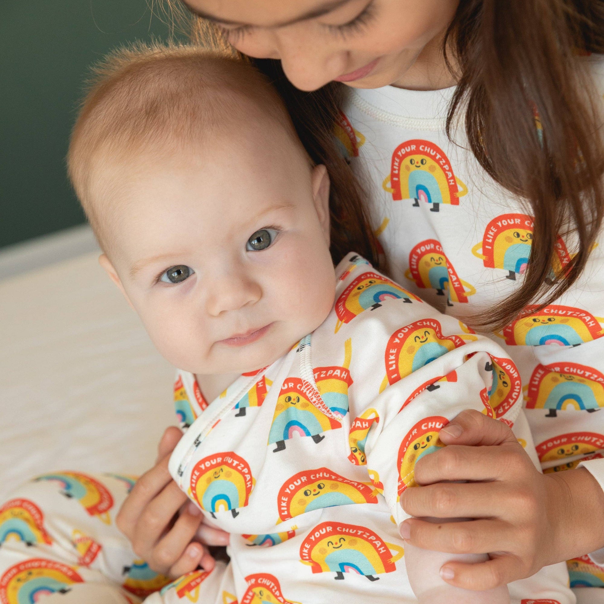 Baby and adult wearing rainbow-patterned pajamas sitting together.