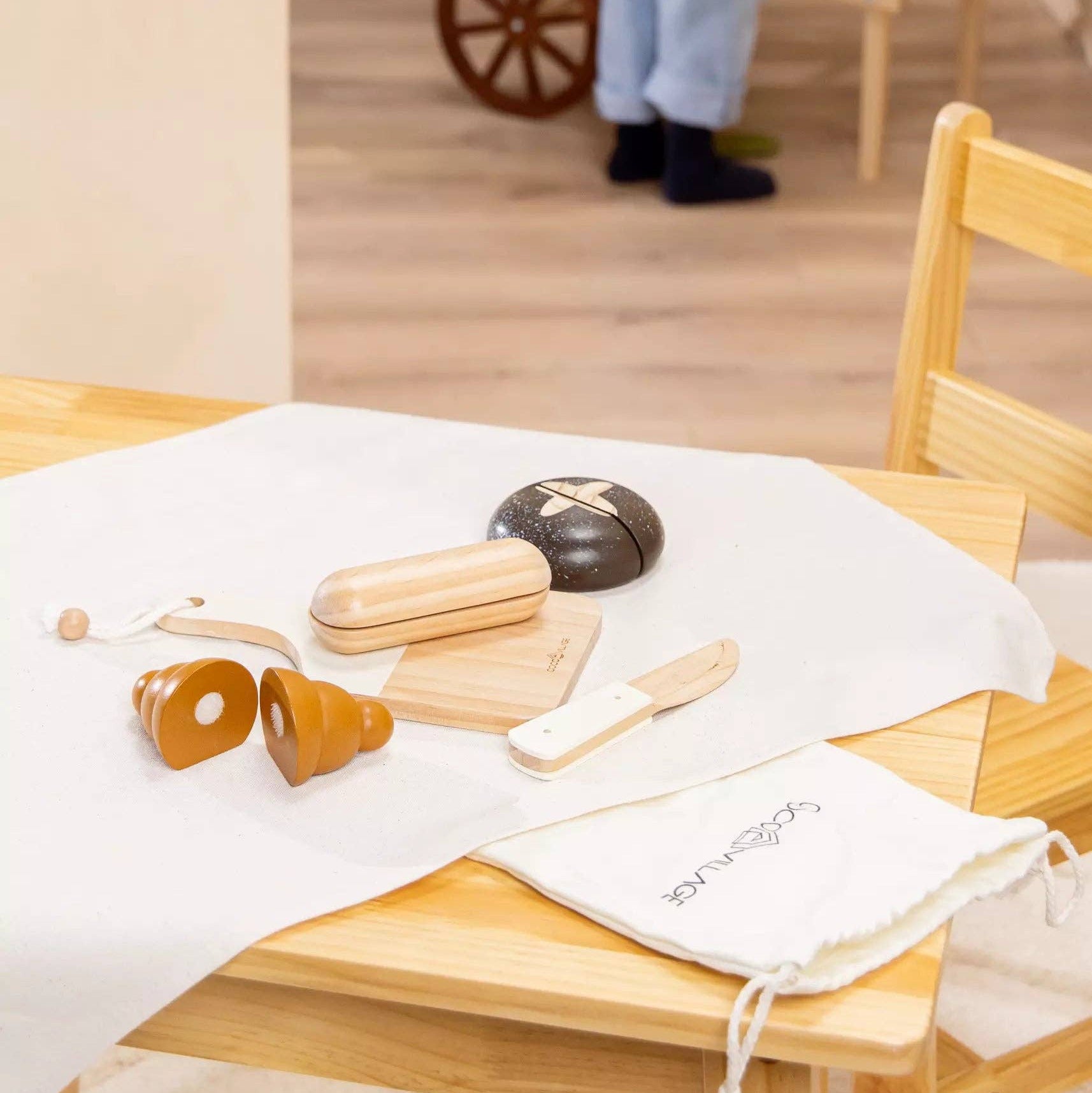 Wooden table with kitchen utensils and a white towel on a light-colored floor.