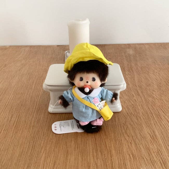 Plush toy resembling a character with a yellow raincoat and blue outfit standing next to a white toilet on a wooden floor.