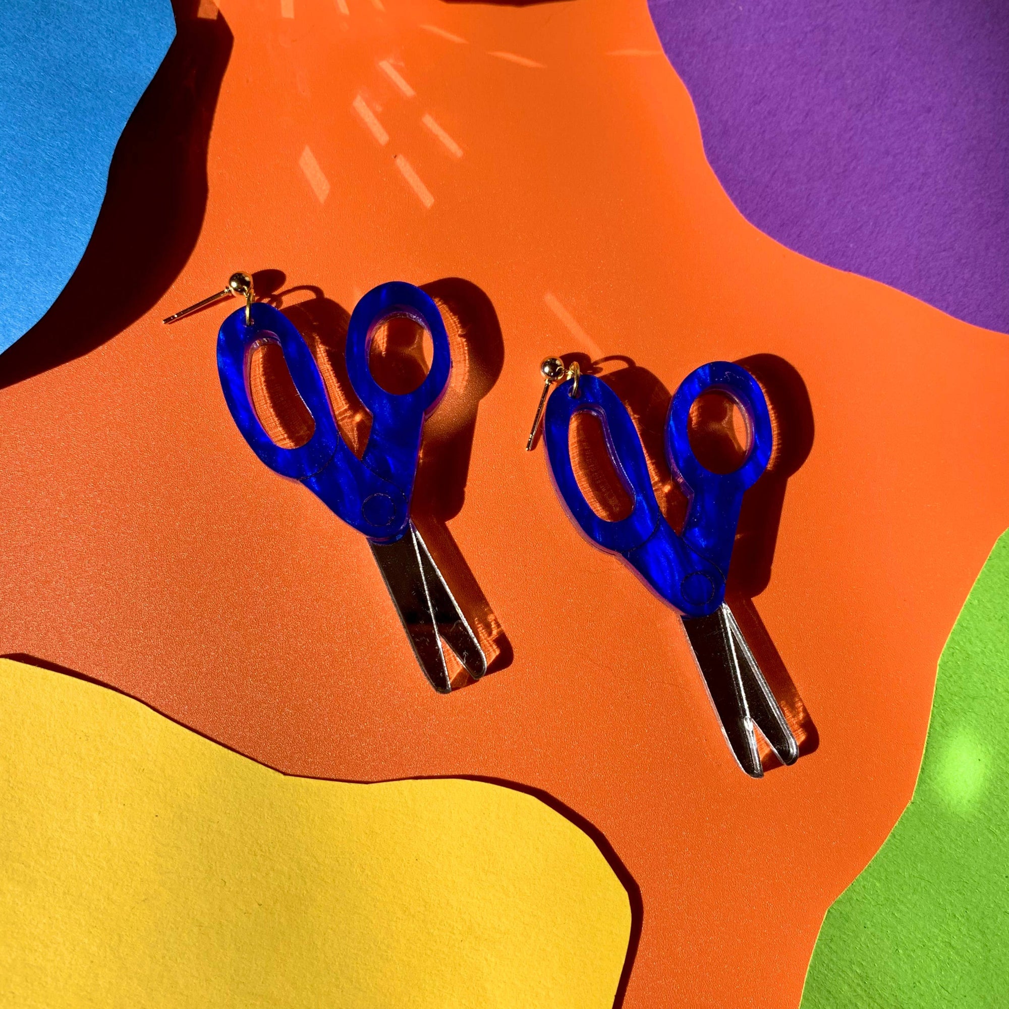 A pair of blue scissors-shaped earrings displayed on a colorful background.