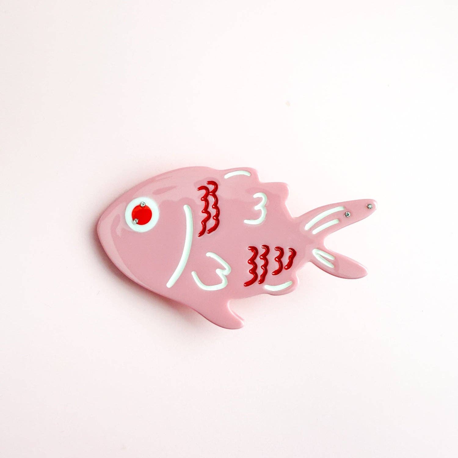 Pink fish-shaped object with red and white design on a light pink background
