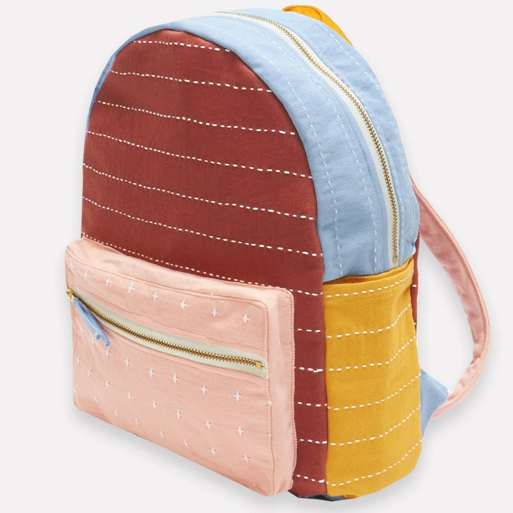 Multicolored backpack with a mix of brown, blue, pink, and yellow patterns on a white background.