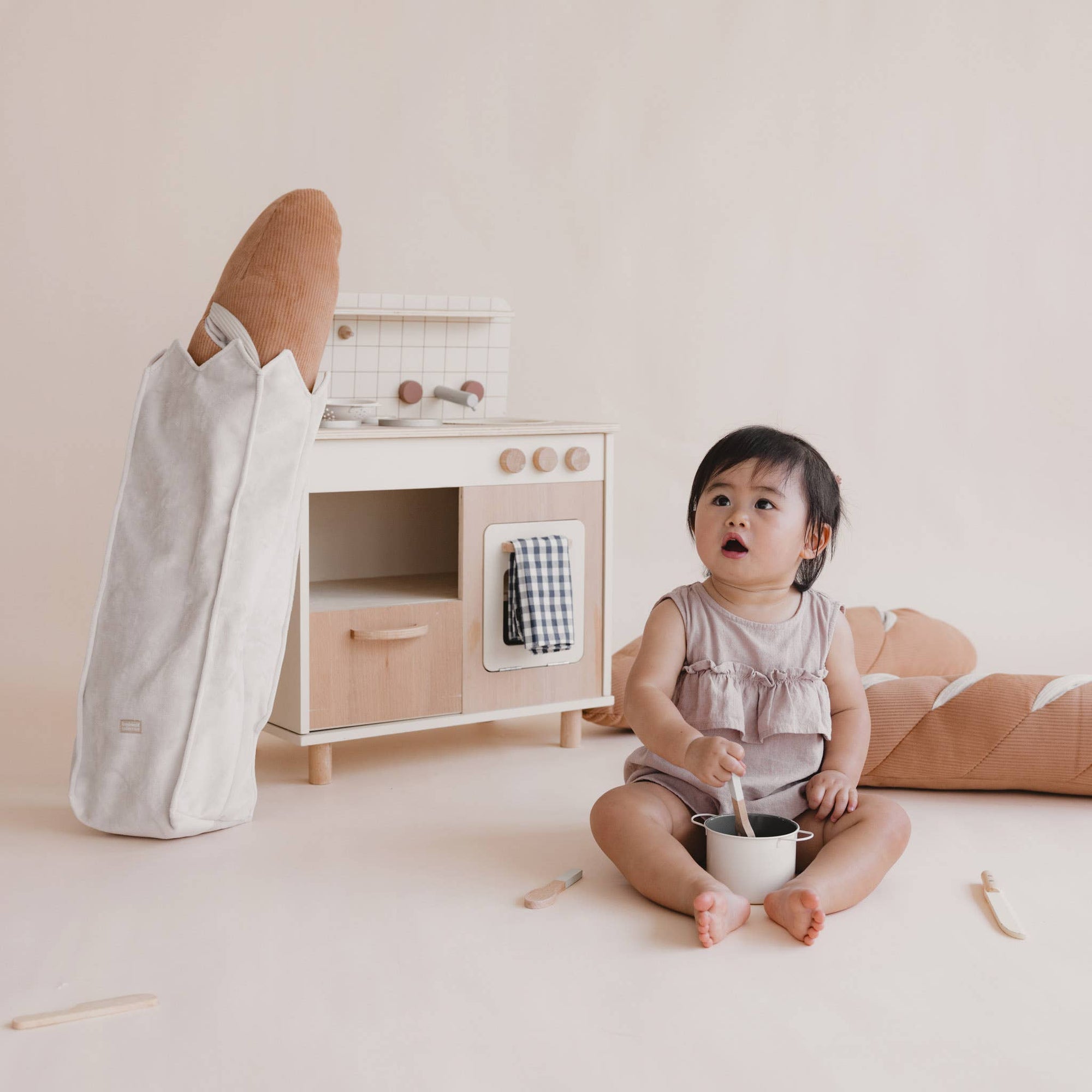 Child playing with a toy kitchen set on a light-colored floor.