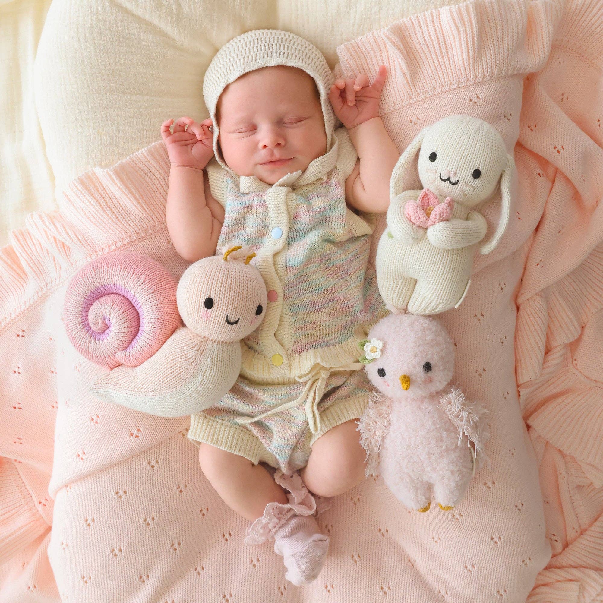 Newborn baby surrounded by soft toys on a pink blanket
