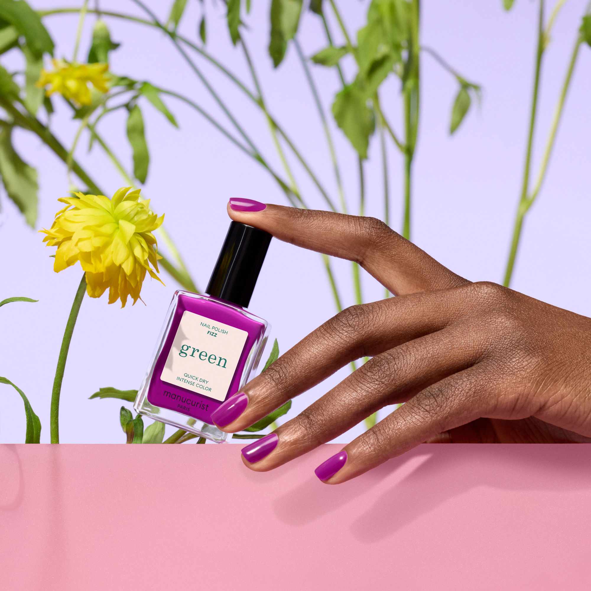 Hand holding a purple nail polish bottle with green label against a floral background