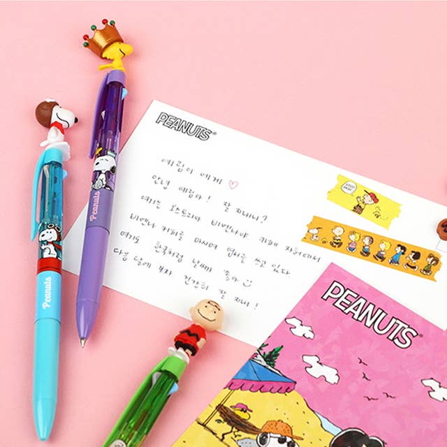 Three colorful pens with cartoon characters on a pink background with Peanuts-themed stationery.