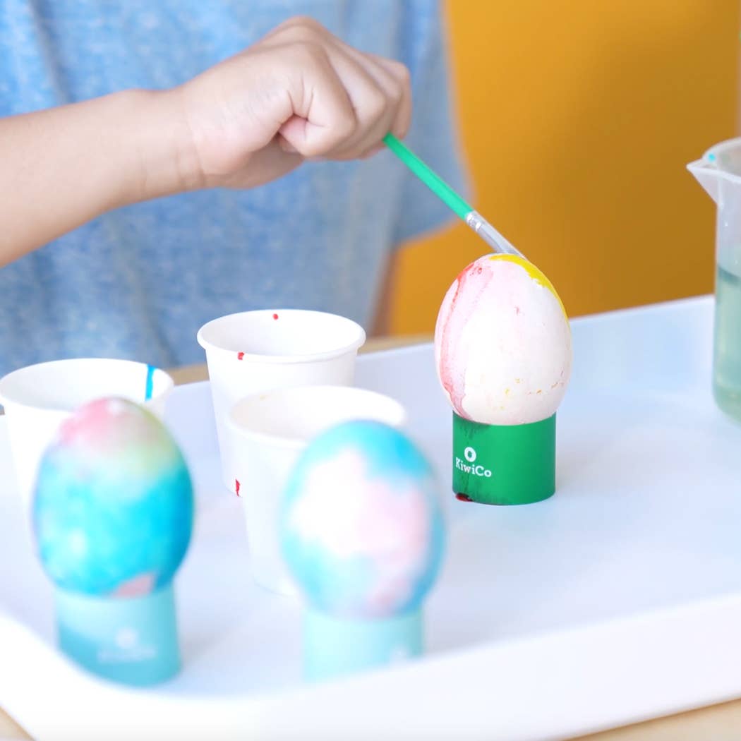 Colorful bath bombs being painted with a brush on a white surface.