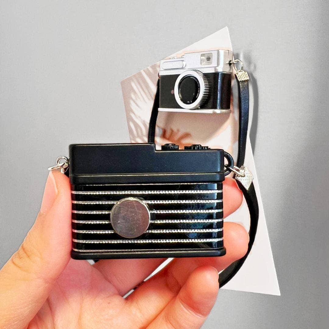 Hand holding a black and silver camera with a strap, against a gray background