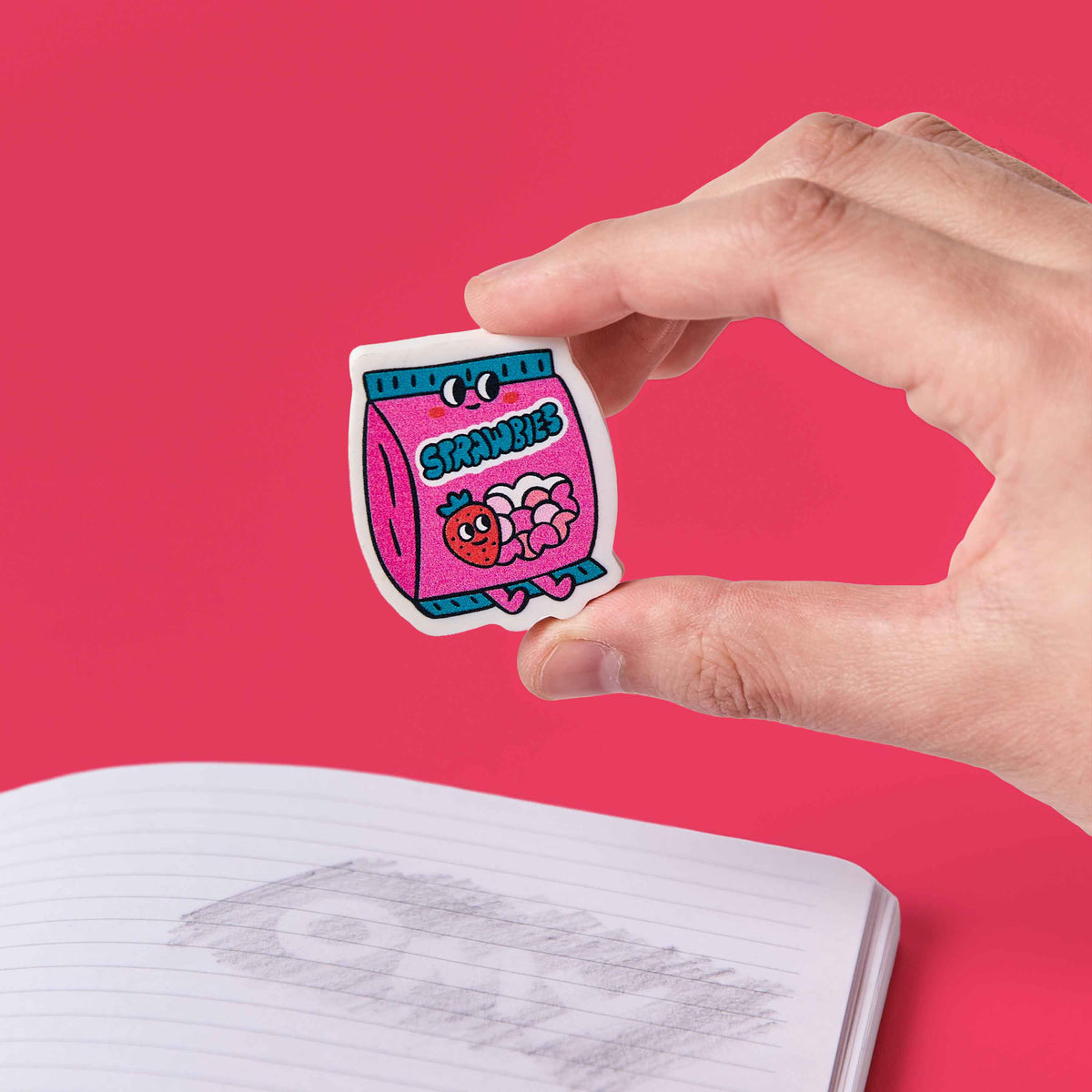 Hand holding a colorful sticker over an open book with a pink background