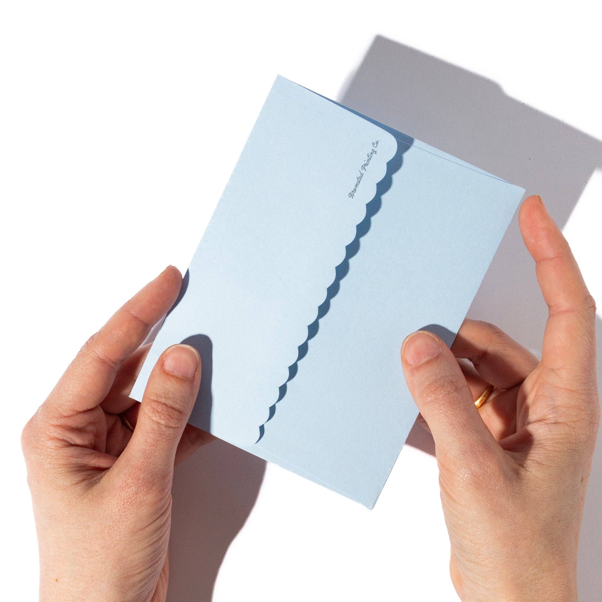 Hands holding a light blue card with a wavy edge design on a white background