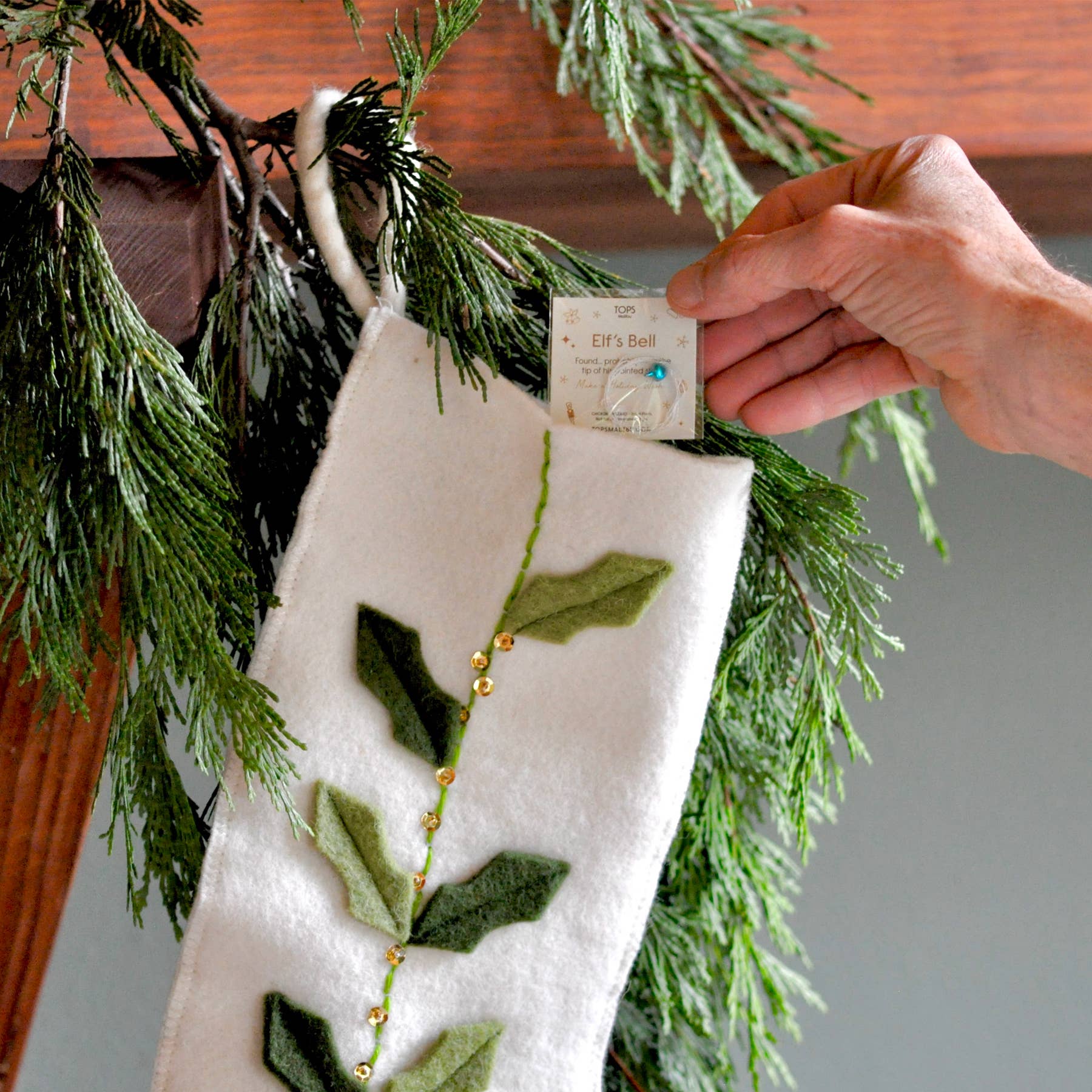 Hand placing a card on a decorative stocking with green leaf patterns against a wooden background.