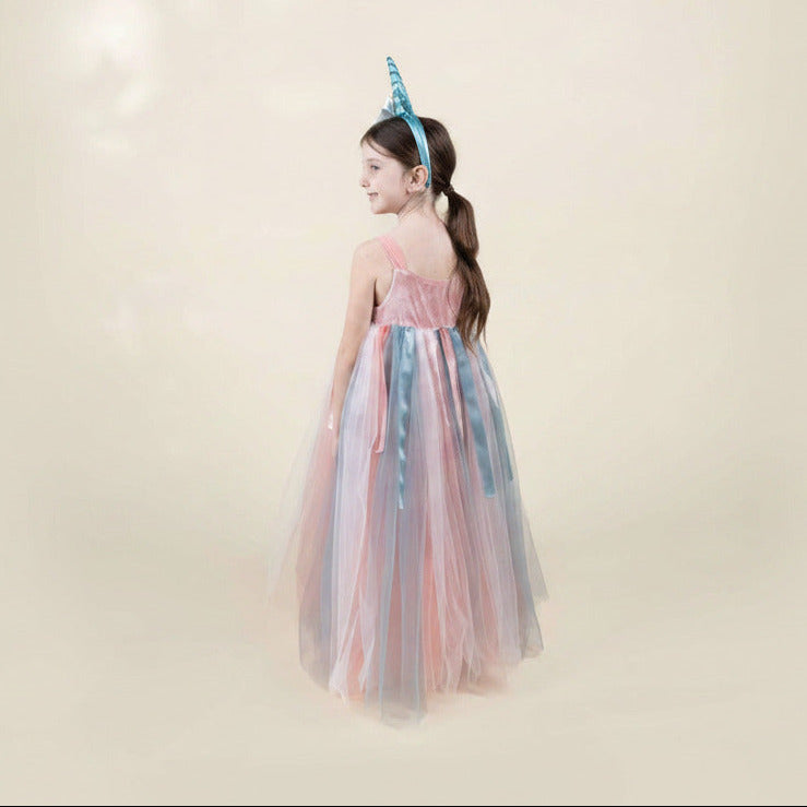 Young girl in a colorful dress with a unicorn horn headband on a plain background