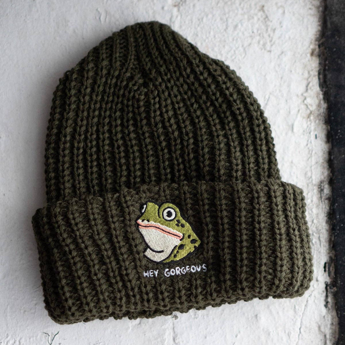 Green knit beanie with a frog design and text on a textured white background