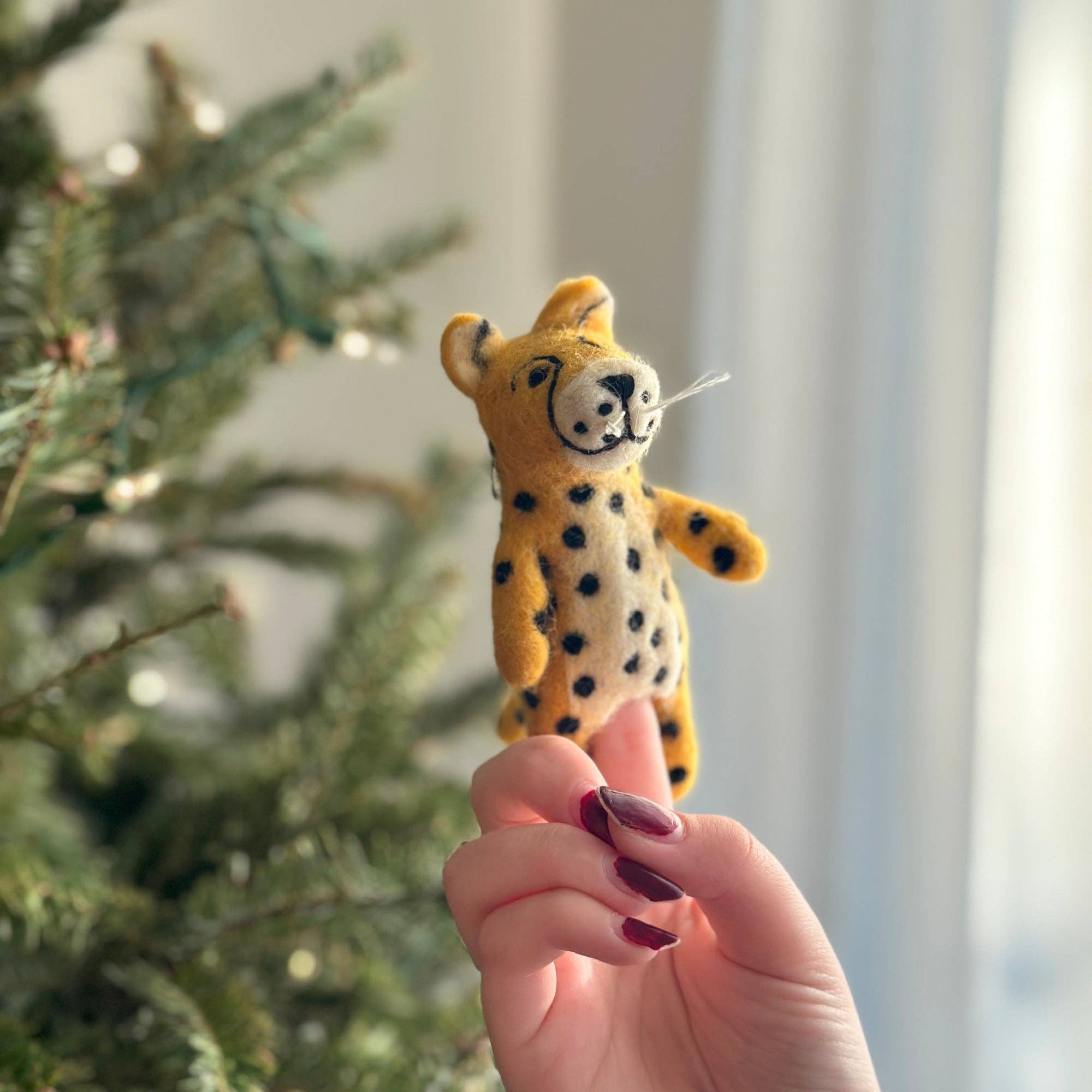 Hand holding a small cheetah figurine in front of a blurred Christmas tree.