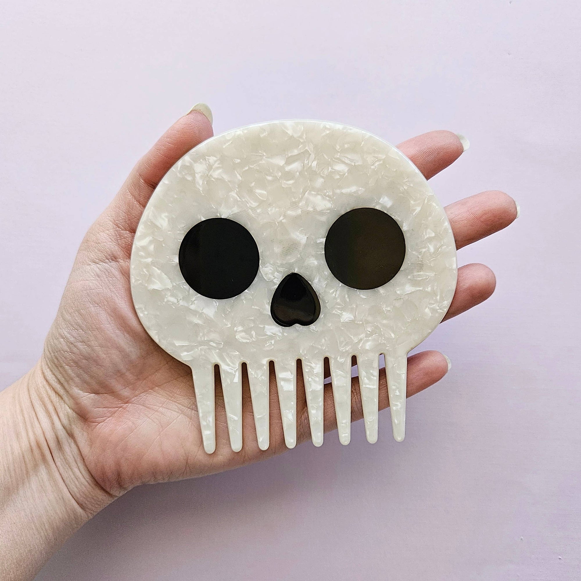 Skull-shaped comb held in a hand against a light purple background