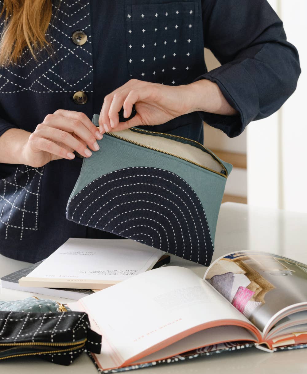 Person holding a blue pouch with white stitching over open books