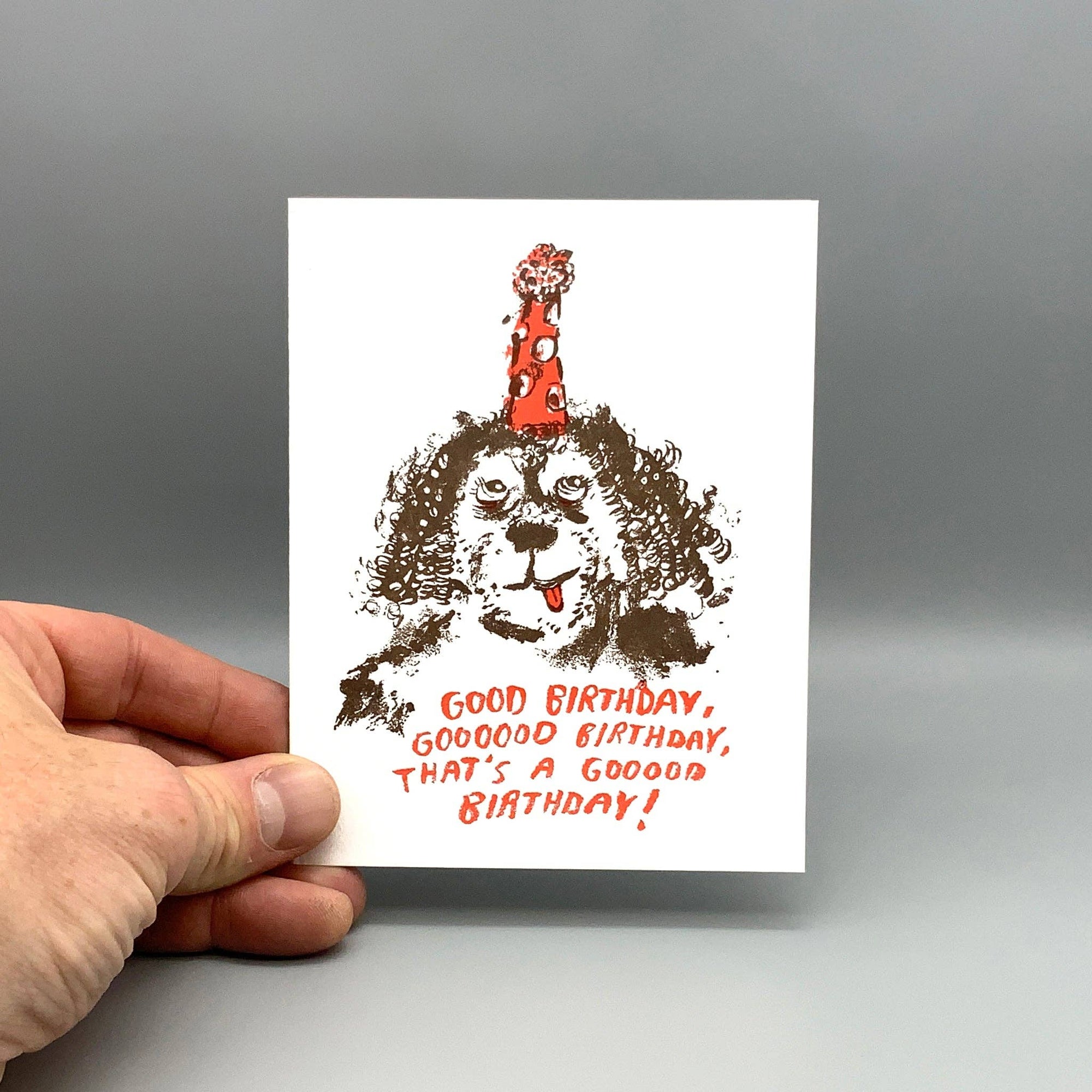 Hand holding a birthday card with a dog illustration and text on a gray background
