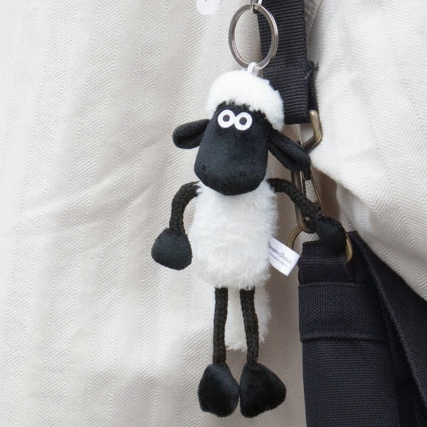 Plush sheep keychain attached to a strap with a beige background