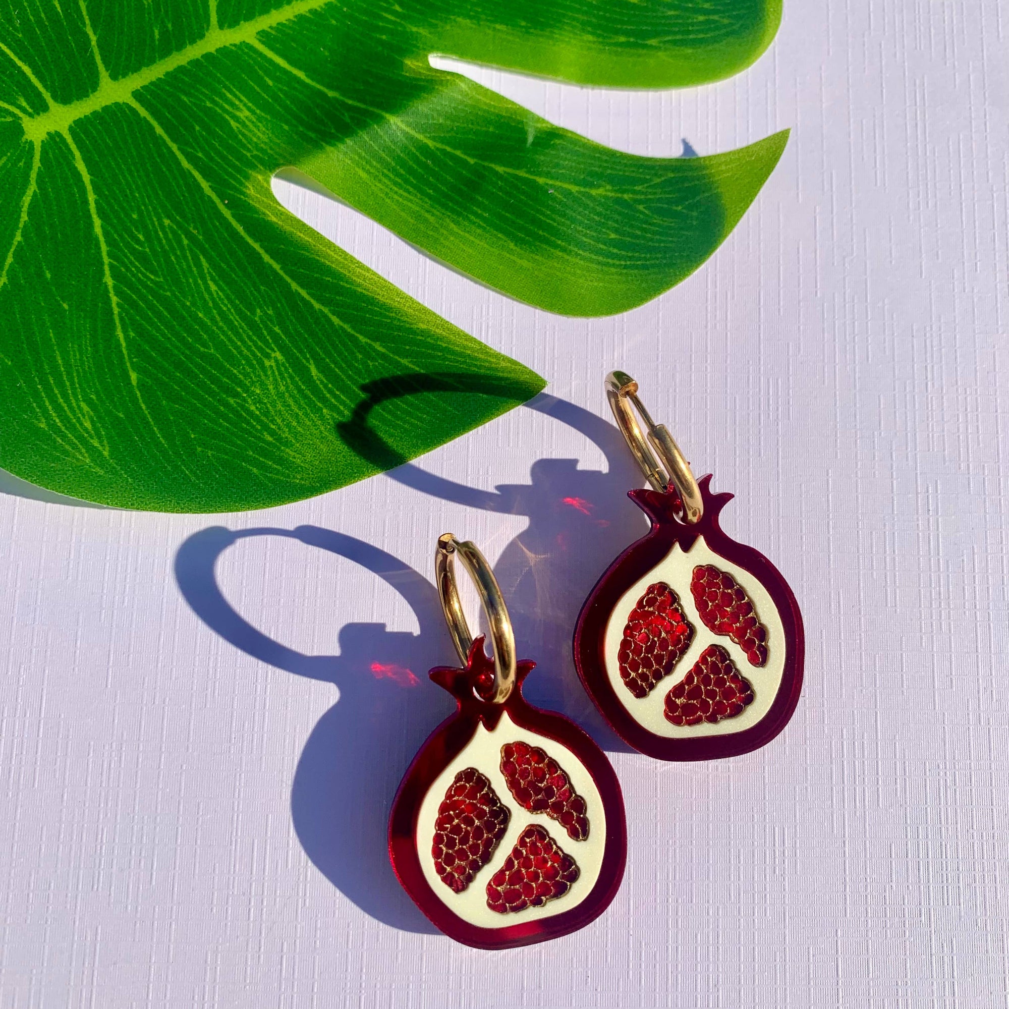 Pomegranate-themed earrings on a white background with a green leaf