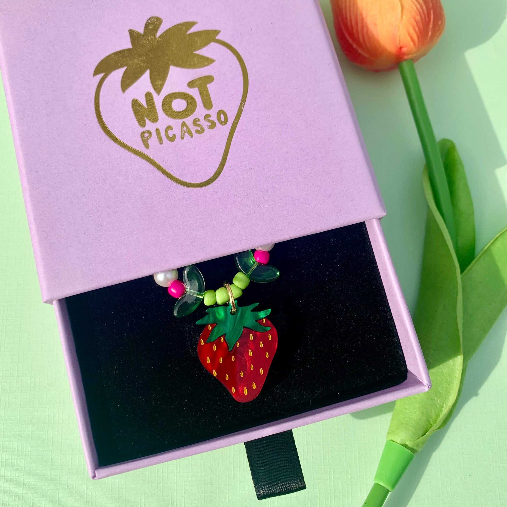 Strawberry-shaped pendant in a 'Not Picasso' box with a tulip on a light green background