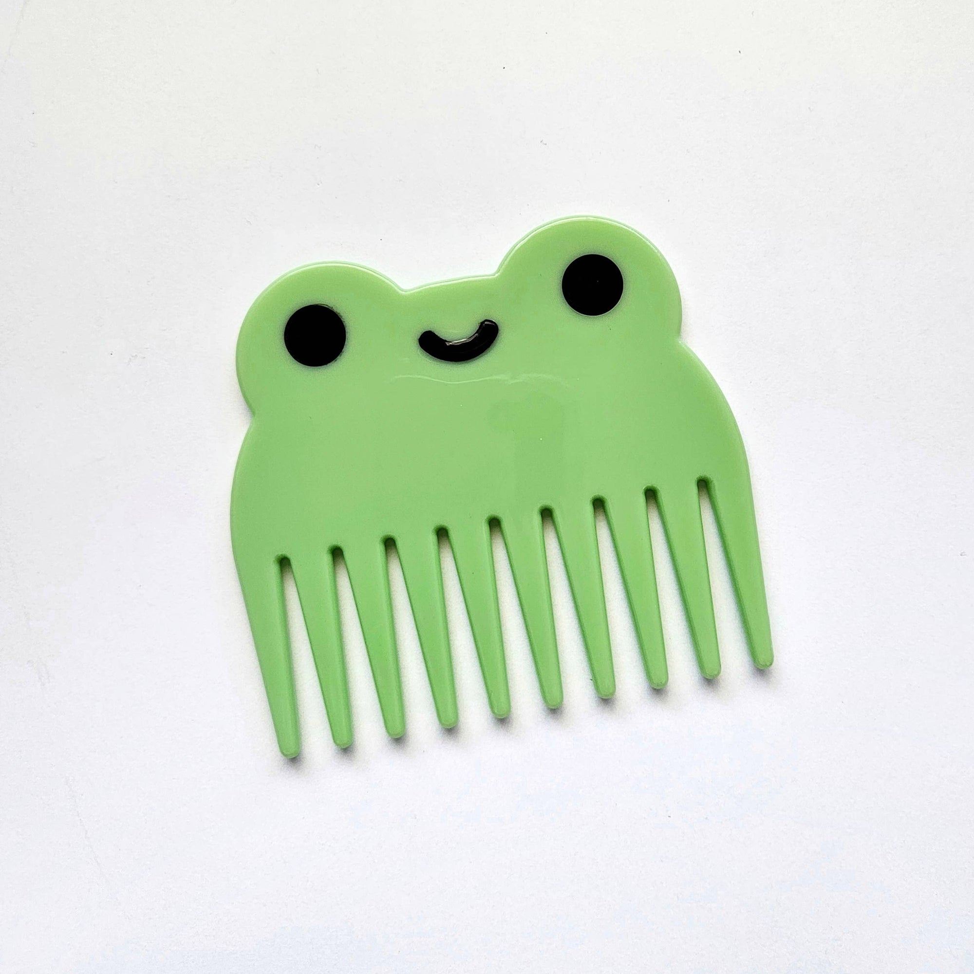 Green comb shaped like a frog with black eyes and a smile on a white background