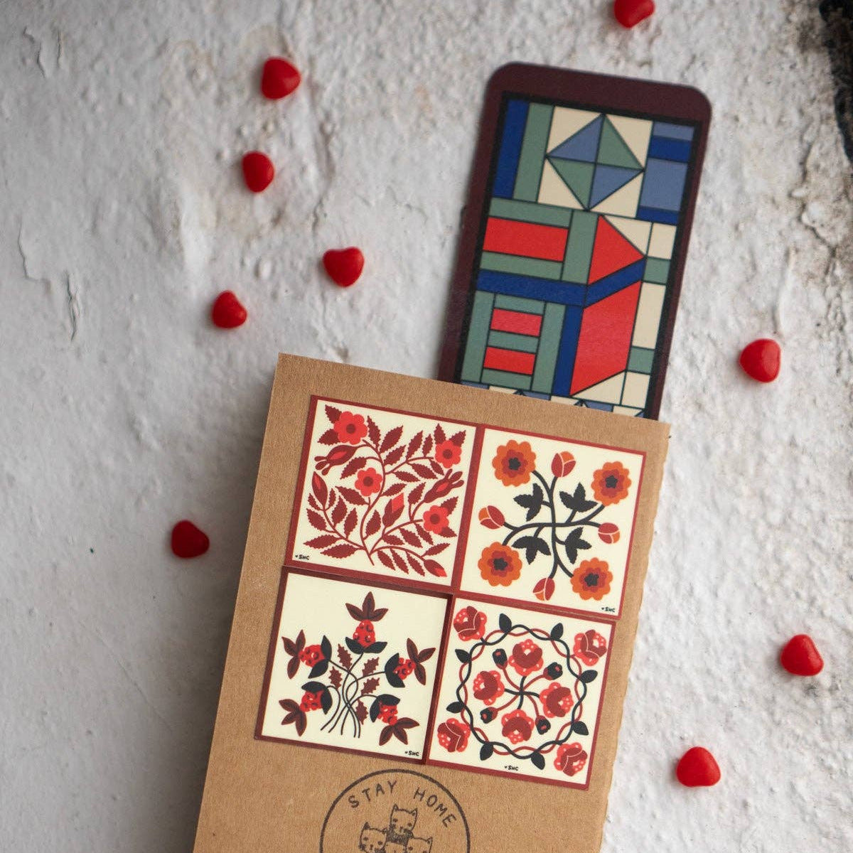 Cardboard box with floral designs and a geometric card on a textured white surface with red heart-shaped objects.