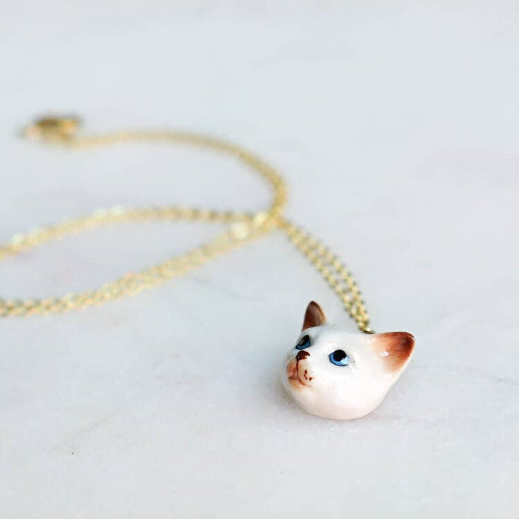 Cat-shaped pendant on a gold chain against a light background