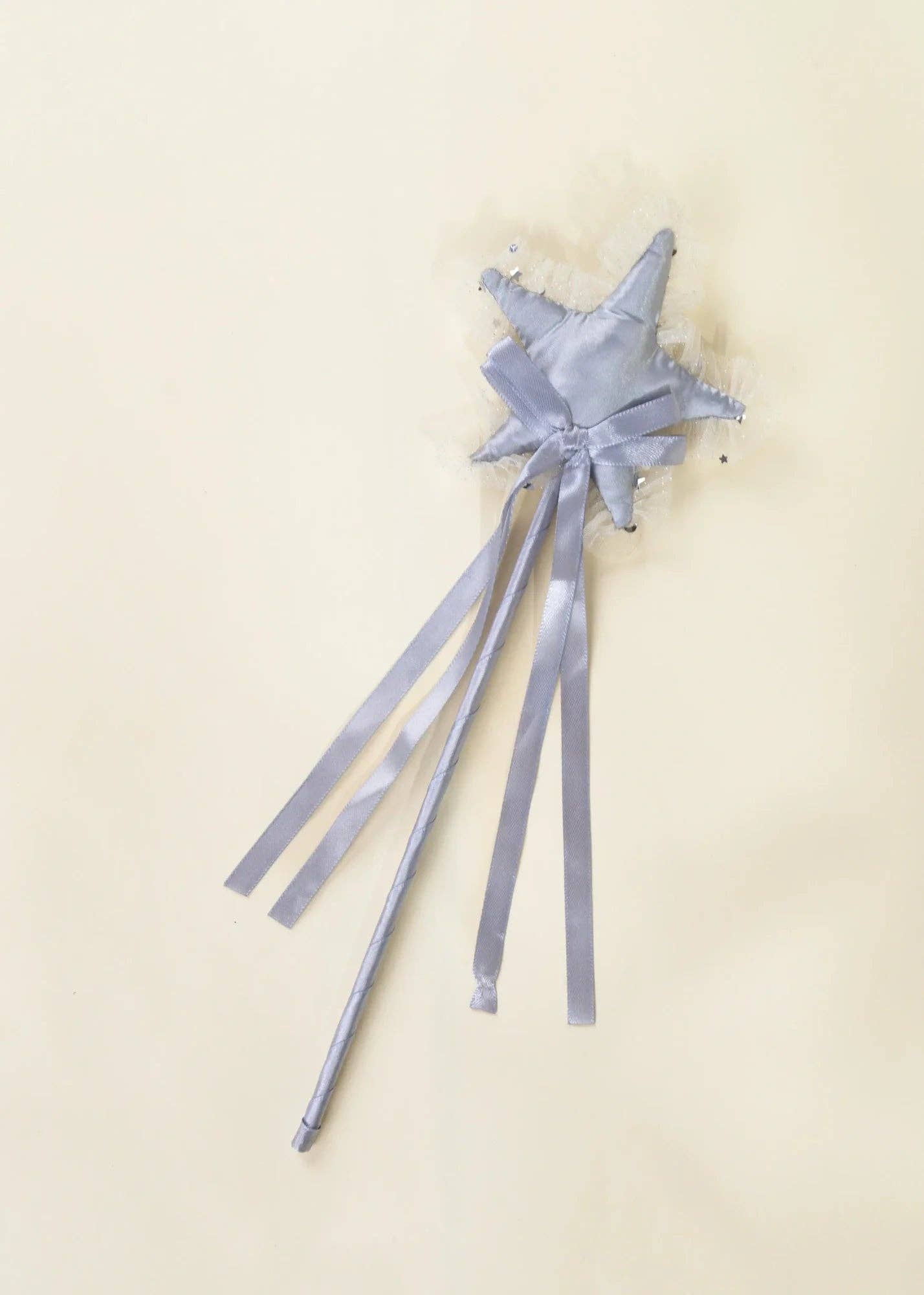 A silver fabric star wand with long flowing ribbons, displayed on a plain cream-colored background.