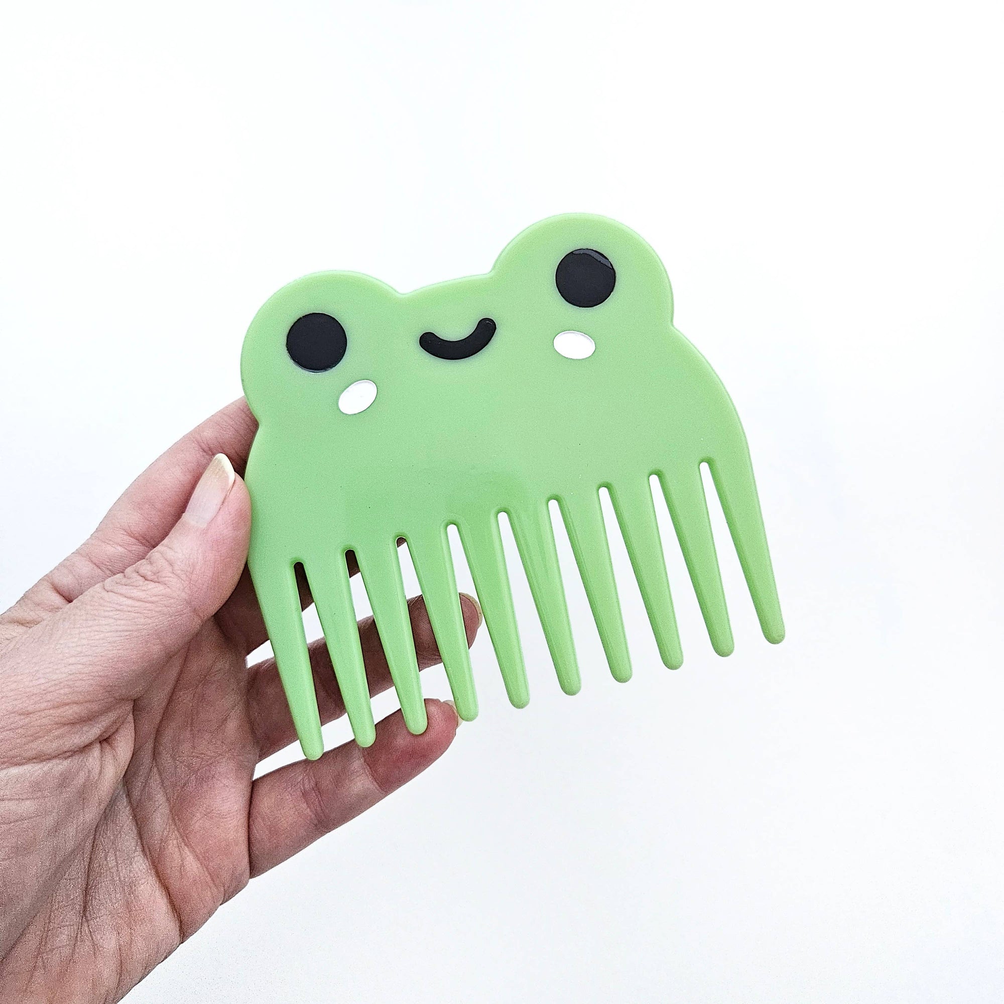 Green comb shaped like a smiling face held by a hand on a white background