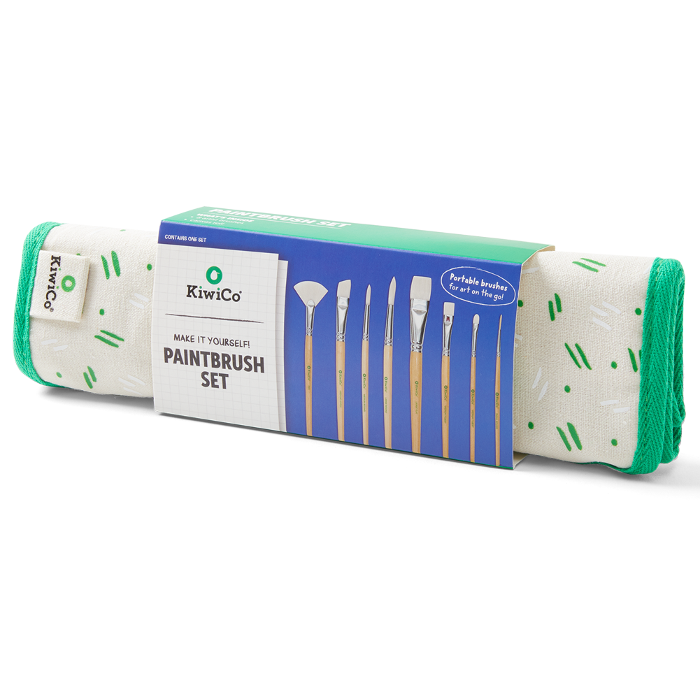 KiwiCo Paintbrush Set in a green and blue cardboard sleeve, showing the rolled white fabric bristles with green accents and wooden handles.