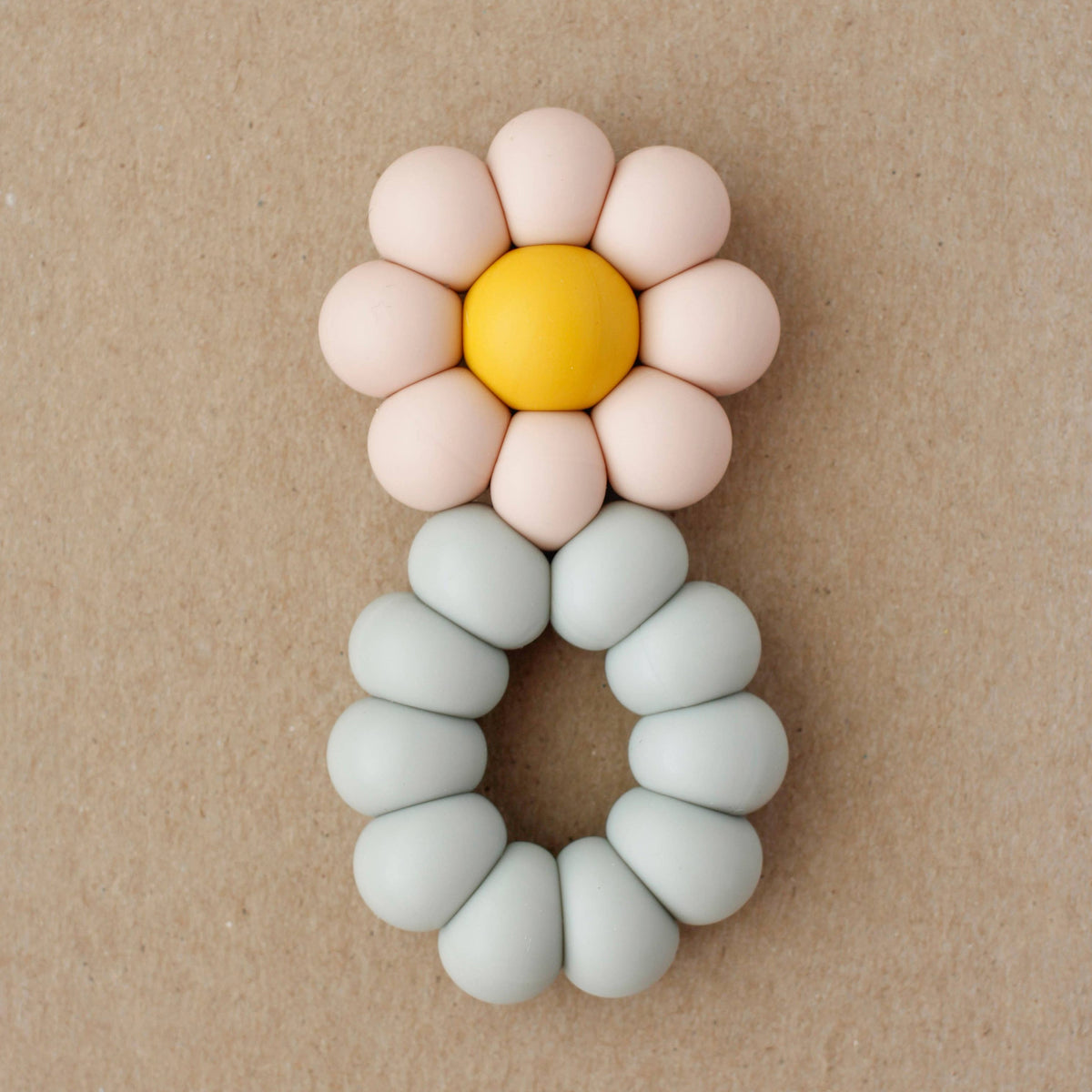 Flower-shaped teething ring with pink petals and a yellow center on a beige background