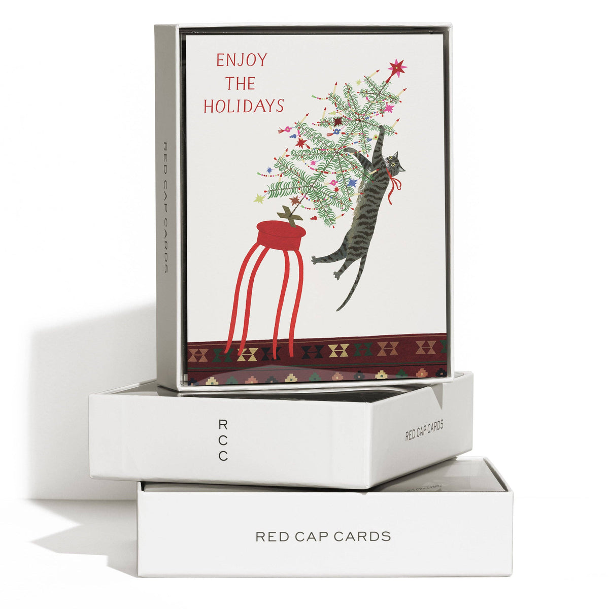 A boxed holiday greeting card set displayed on a white background. The top card shows an illustration of a gray tabby cat climbing a decorated Christmas tree next to a red hanging chair, with the text 'ENJOY THE HOLIDAYS.