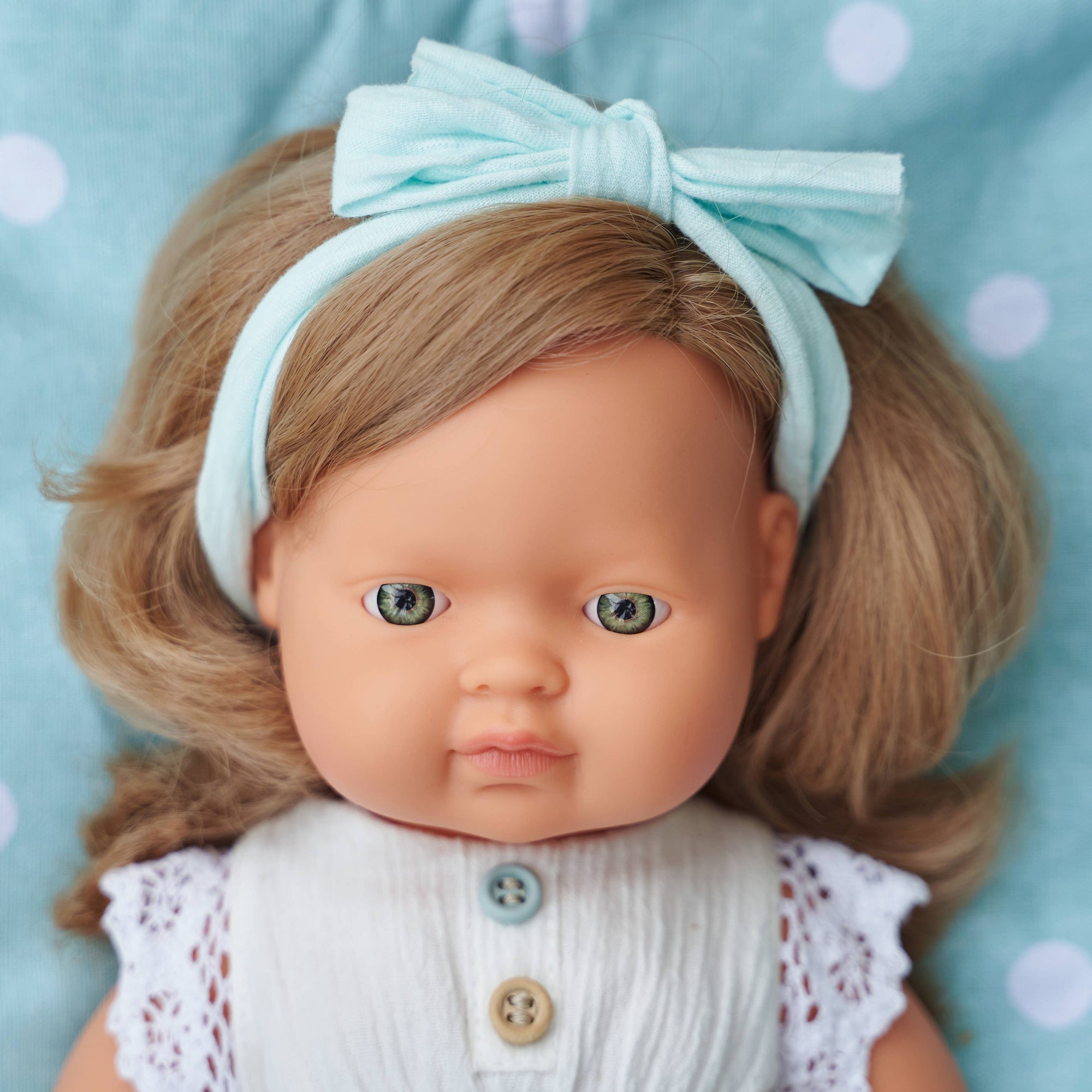 Doll with a light blue bow headband on a polka dot background