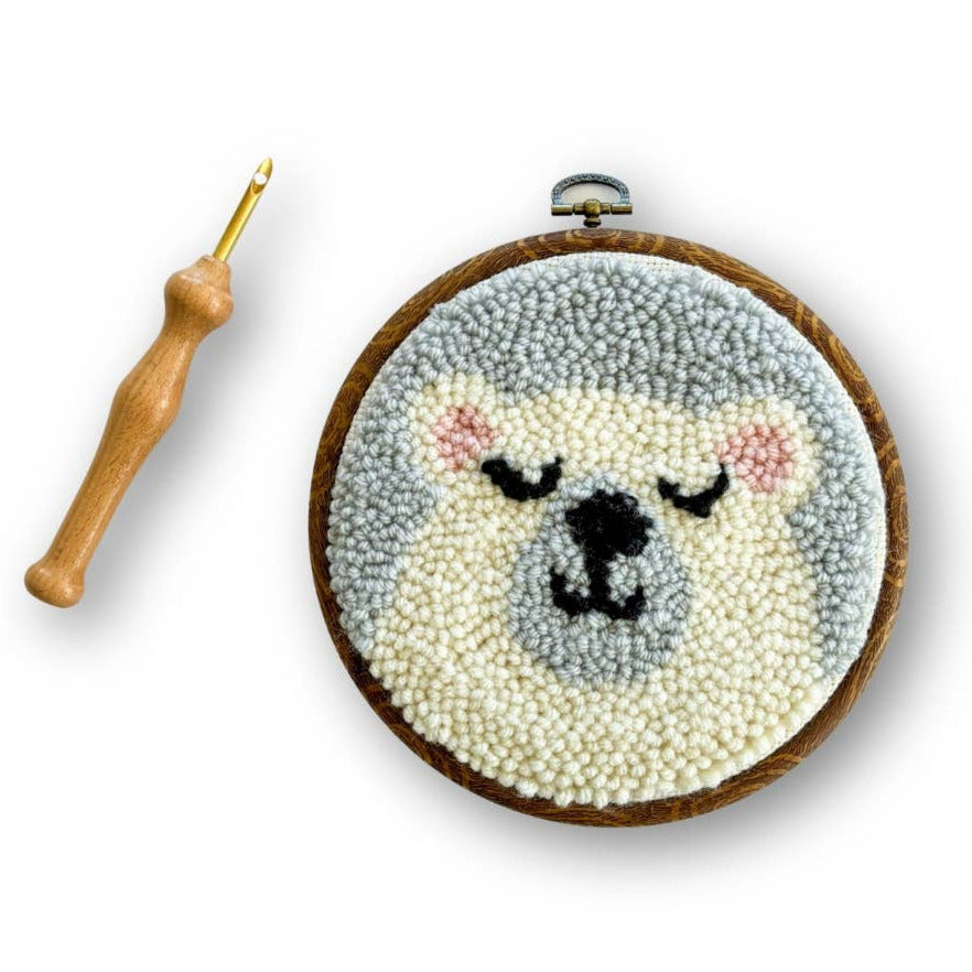 Embroidery hoop with a sleeping bear design and a crochet hook on a white background