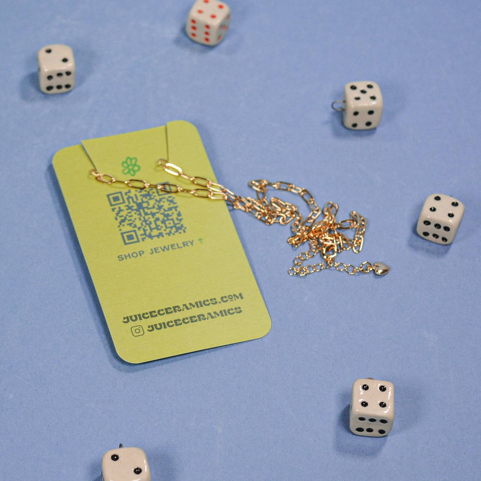 Green jewelry card with gold chain and QR code, surrounded by dice on a blue background