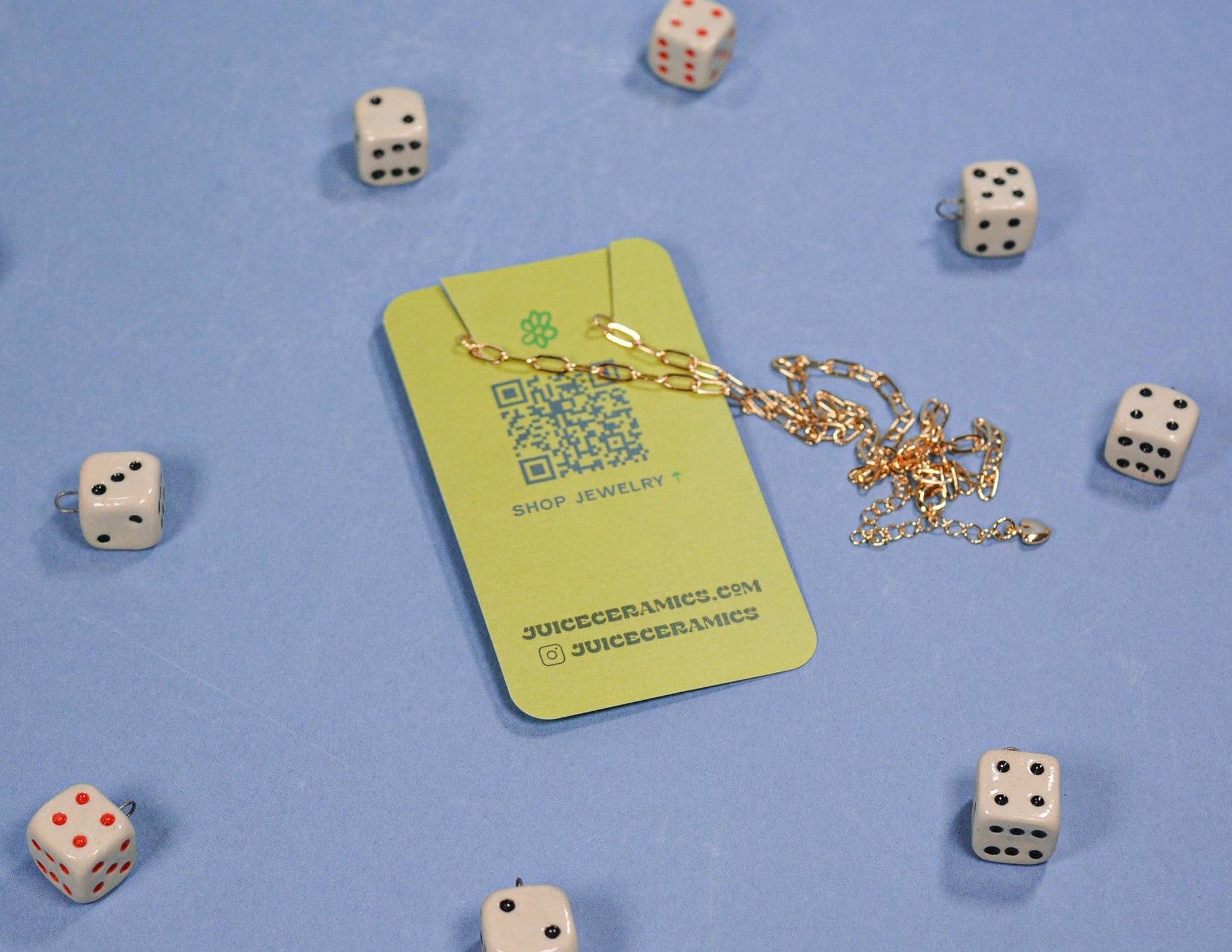 Green jewelry card with gold chain and QR code, surrounded by dice on a blue background