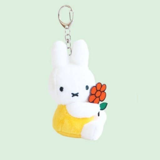 Plush keychain of a white rabbit holding an orange flower on a light green background